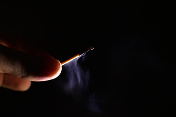 fingers holding an extinct smoking match on a black background
