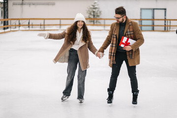 Smiling couple having fun in a figure skating field with a present