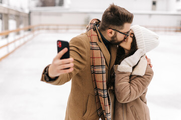 Happy couple taking a selfie in a figure skating field and kissing