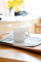 White coffee mug with napkin on table in real kitchen interior with bright natural sunlight