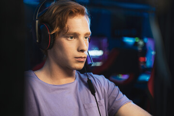 Player with headphones playing at popular online game while sitting with serious face