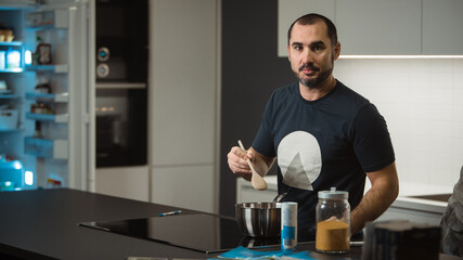 Young man is cooking dinner or a meal in a fancy big kitchen. Hipster guy cooking in a white kitchen.