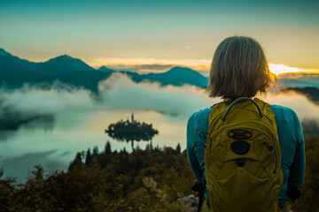 Short haired female hiker is waiting and observing morning sunrise over the lake of Bled and the...