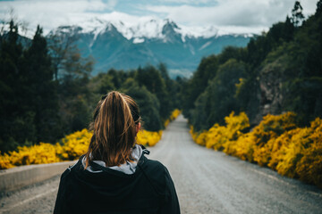 Close up back view of a woman waling alone in a mountain road with Los Andes on the background. - obrazy, fototapety, plakaty