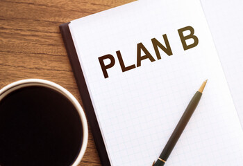 Plan B text in a notepad next to a cup of coffee, a pencil and glasses on the wooden desk