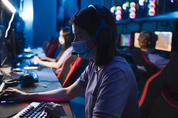 Fototapeta na wymiar Female e sports player in a medical mask playing in online shooter on a powerful computer