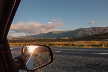 View from a car on a mountains and reflection in a car mirror of a sun rise over mountain peak. Connemara, county Galway, Ireland. Car travel with stunning nature scenery. Sun flare
