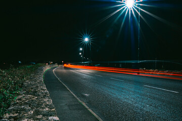 Night scene with car trail on a small narrow road. City lights illuminated with light burst.