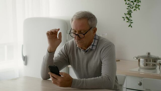 Eyesight Problems Concept. Senior Man Wearing Eyeglasses Reading Message On Smartphone