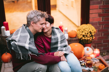 A couple having a romantic date on the porch of their home. Cozy ideas on how to spend time at home. Autumn tea time outdoors on house entrance decorated with pumpkins, flowers and burning candles