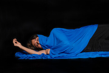 Latin woman with indigenous characteristics standing covering her body with a large blue cloth on a black background