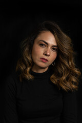 Naklejka premium Dramatic portrait of a Latina woman with serious or arrogant expression looking straight into the camera over black background