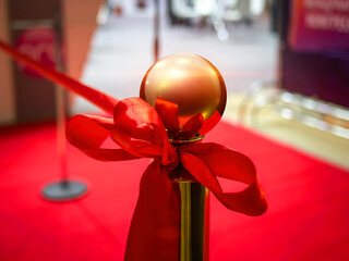 Opening ceremony of an event. A red festive satin ribbon tied to a gold post. Ribbon cutting...
