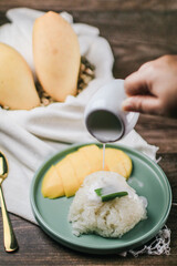 Delicious mango sticky rice serve with coconut milk on wooden table. Popular traditional dessert of Thailand.