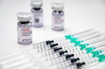 Coronavirus vaccination against SARS-CoV-2. Medical syringes, each with a dose of COVID-19 vaccine, and several glass vials in the background.