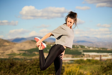 young woman stretching before training on road with mountains and clouds in the background