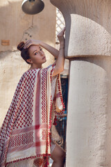red-haired beautiful girl in Arabic clothes stands against the background of the old arabic city, bazaar. dressed in a beige abaya with embroidery and a scarf on her head