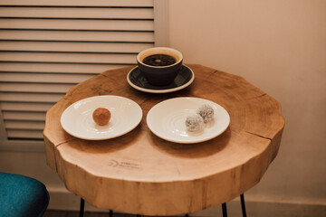 On a wooden table is a cup of coffee and sweets on saucers
