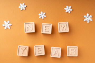 The inscription new year on wooden cubes. Wooden cubes with letters and snowflakes on an orange background. New Year's card