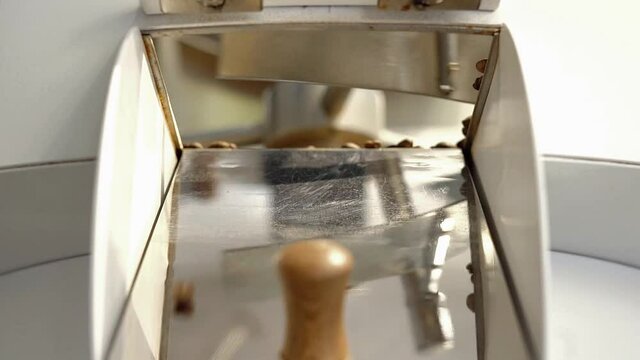 beans spilled from coffee machine. Freshly roasted coffee beans on a cooling tray, being mixed by a rotating mechanical arm, then being emptied.