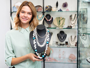 Young smiling salesgirl offering natural gemstone jewelry in boutique, showing elegant pearl...