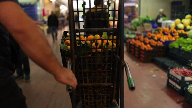 fruit and vegetable market. worker carrying crate of tangerines with wheelbarrow