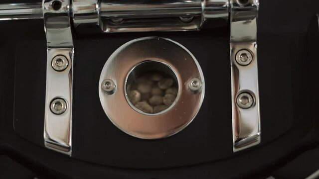 mixing roasted coffee beans in roaster machine. Coffee beans are roasted in a roaster. Through the transparent panel, grains are visible, which are constantly being mixed