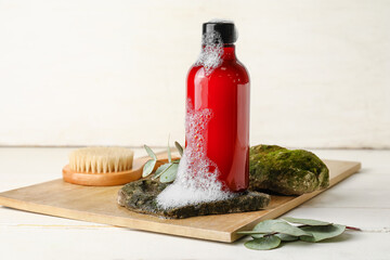 Board with bottle of shower gel, massage brush and stones on wooden table