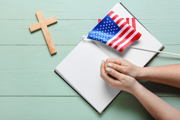 Fototapeta premium Woman with Holy Bible, USA flag and cross on green wooden background