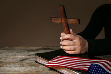 Woman with cross, Holy Bible and USA flag on dark wooden background