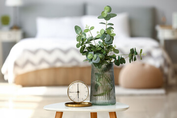 Stylish alarm clock and vase with eucalyptus on blurred room interior background © Pixel-Shot
