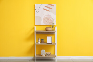 Modern shelf unit with different decor near yellow wall in room