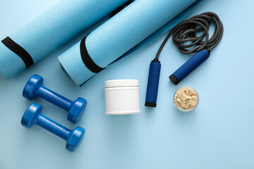 Bowl with protein powder, jar, fitness mats, dumbbells and skipping rope on color background