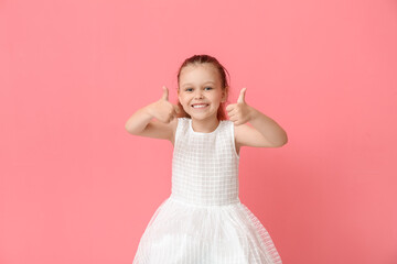 Portrait of pretty little girl showing thumb-up on color background