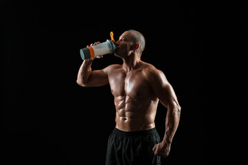 Male bodybuilder drinking protein shake on dark background