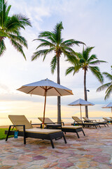 Umbrella and chair around swimming pool in hotel resort with sunrise in morning