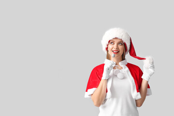 Beautiful young woman in Santa costume and with lollipop on grey background
