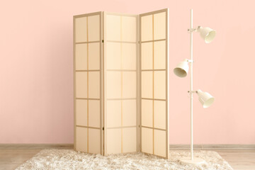Stylish folding screen and floor lamp near wall in room