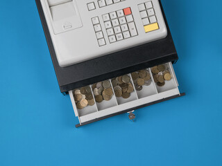 An open cash register filled with coins on a blue background.