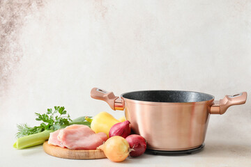 Cooking pot with ingredients for tasty soup on light background