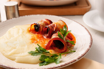 Plate with mashed potatoes, prunes baked in crispy bacon, gravy sauce and parsley on table, closeup