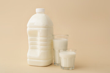 Gallon bottle and glasses of milk on color background