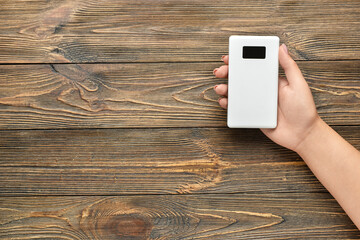 Woman holding modern power bank on wooden background