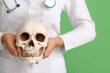 Female doctor with human skull on color background, closeup