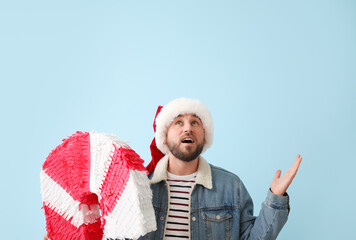 Surprised handsome man in Santa hat with candy cane pinata on blue background