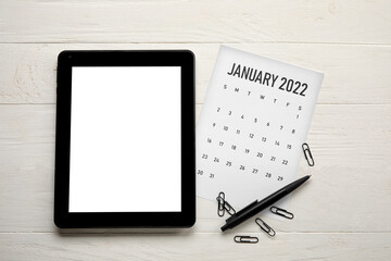 Calendar page of January 2022 and tablet computer on white wooden background