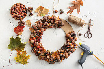 Beautiful wreath made of pine cones and acorns with leaves and scissors on light background