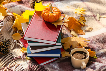 Stack of books, pumpkin, cup of coffee and leaves on plaid in autumn park