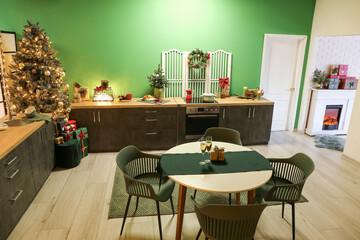 Interior of stylish kitchen with green counters, Christmas tree and dining table