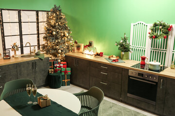Interior of stylish kitchen with green counters, Christmas tree and dining table
